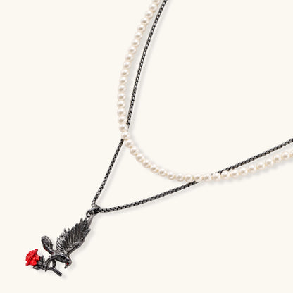 Gothic eagle pendant carrying red rose on black chain layered with white pearls against cream background