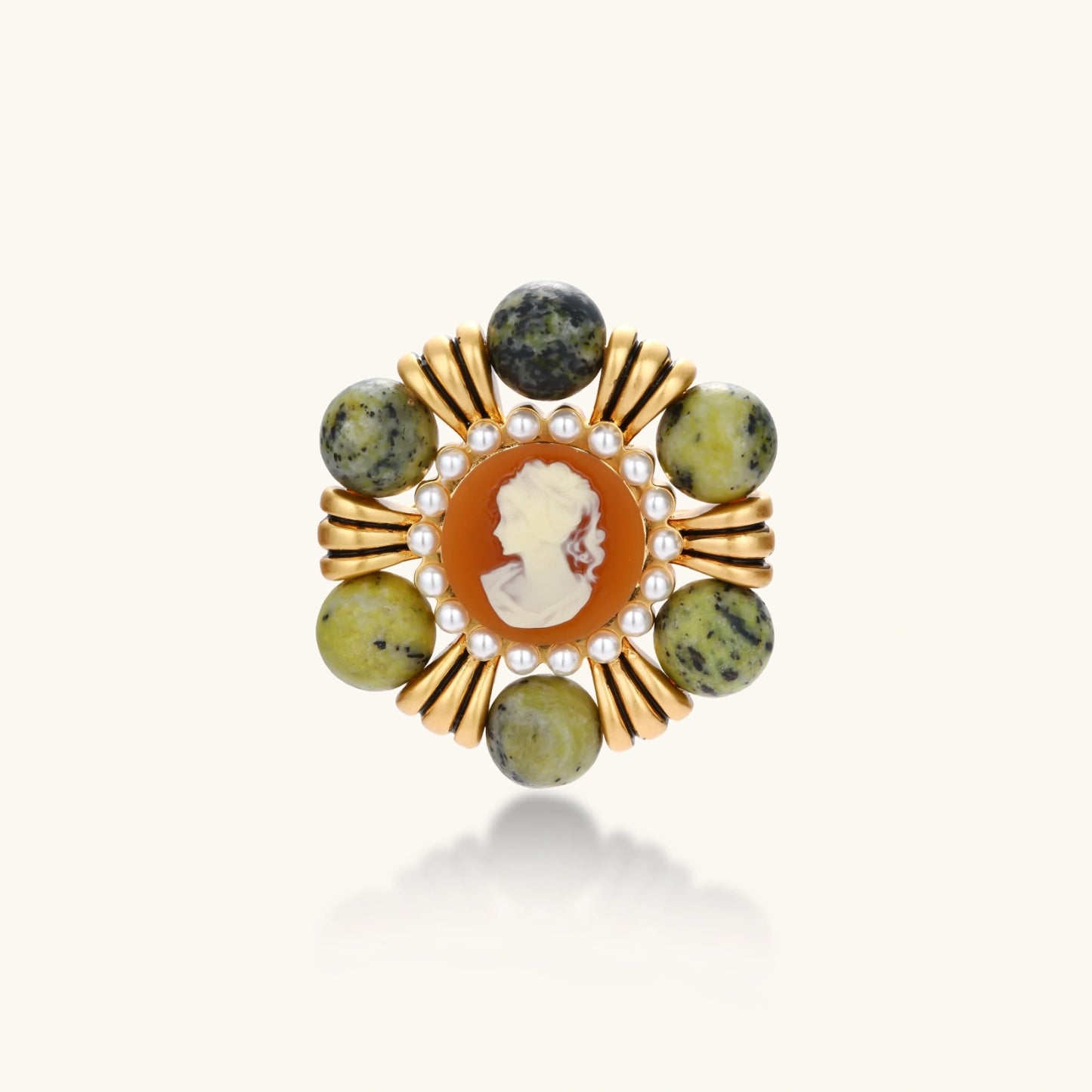 Ornate gold-plated brooch with central cameo, radiating spokes, pearl border, and green marbled natural stones on white background.